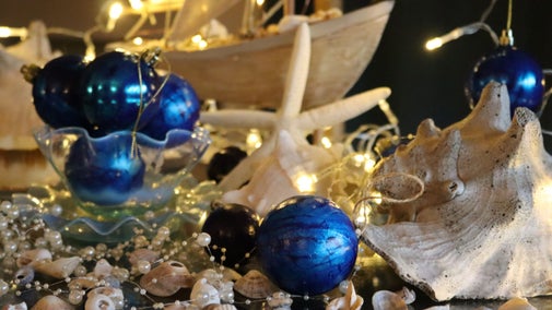 Blue baubles scattered on a table with white shells and starfish, and blurred fairylights in the background.